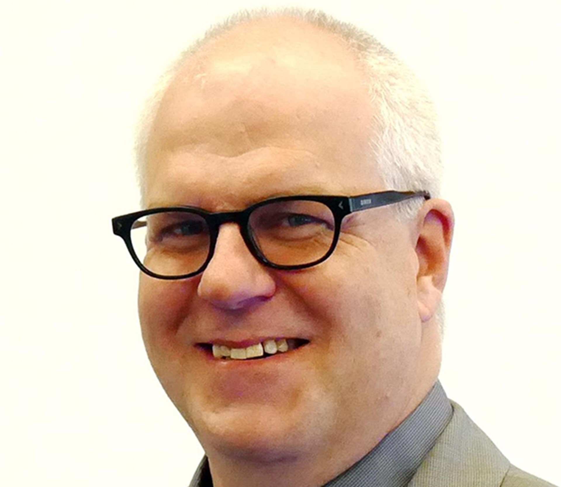 Lächelnder Mann mit weißen Haaren, Halbglatze und schwarzer Brille, der ein dunkelgraues Hemd und eine hellgraue Anzugjacke trägt