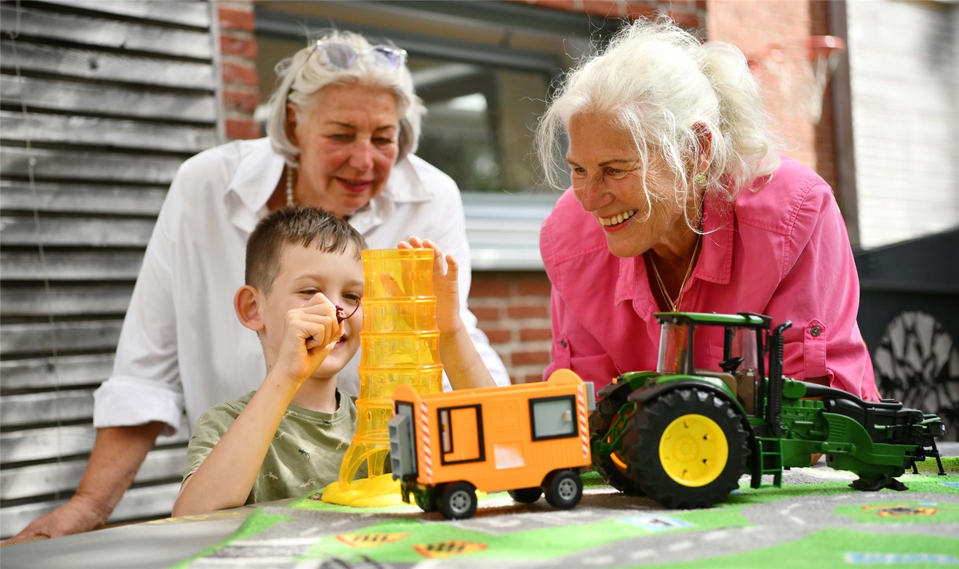 Zwei Frauen spielen mit einem Jungen mit einem Spielzeug-Traktor.