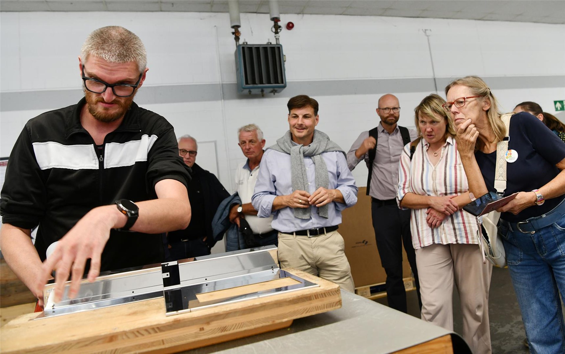 Mann arbeitet mit Holz, eine Gruppe schaut interessiert zu.